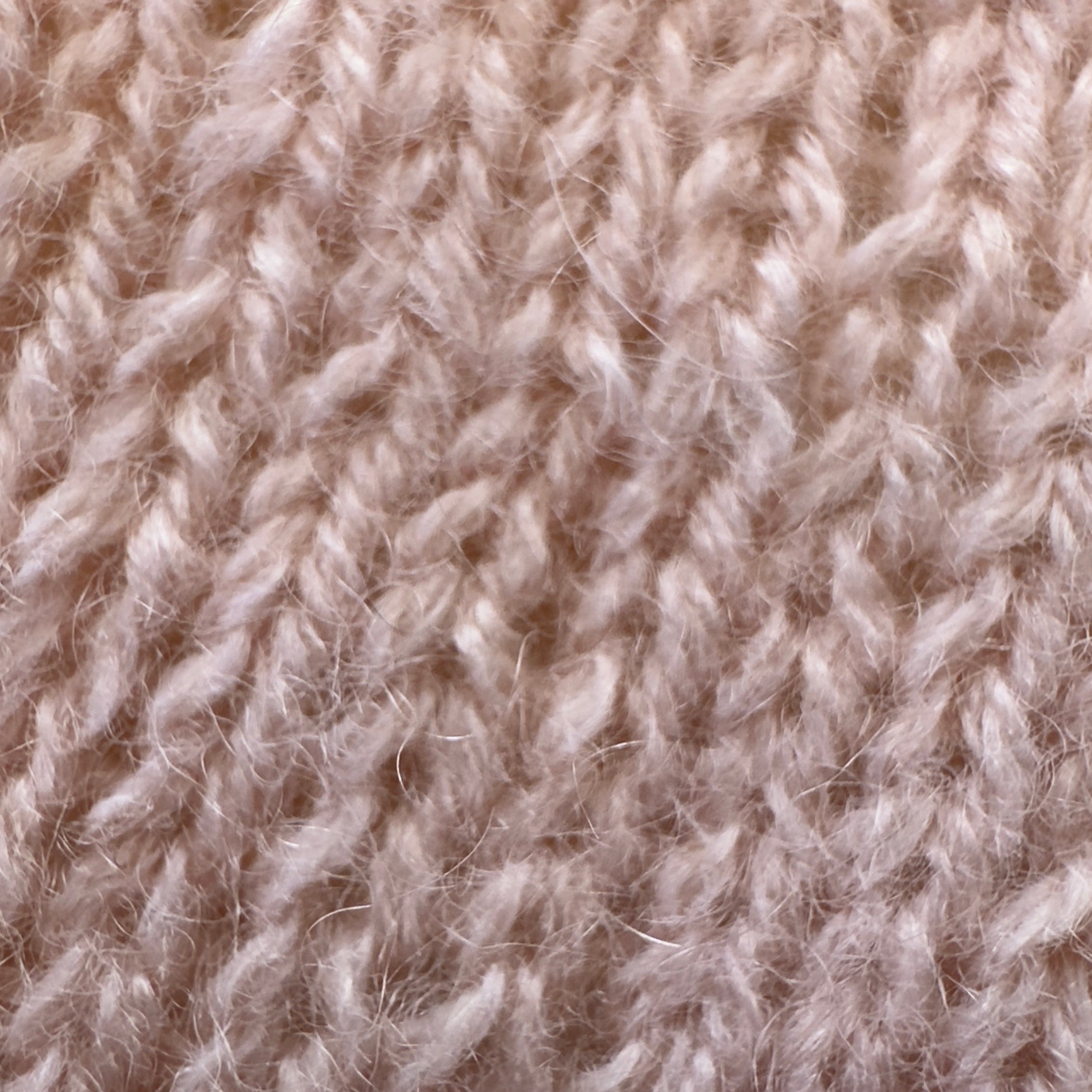 Close-up of knitted reclaimed cashmere yarn in a luminous pastel peach color. The soft halo fo cashmere fibres is shown in a simple knit stitch pattern.