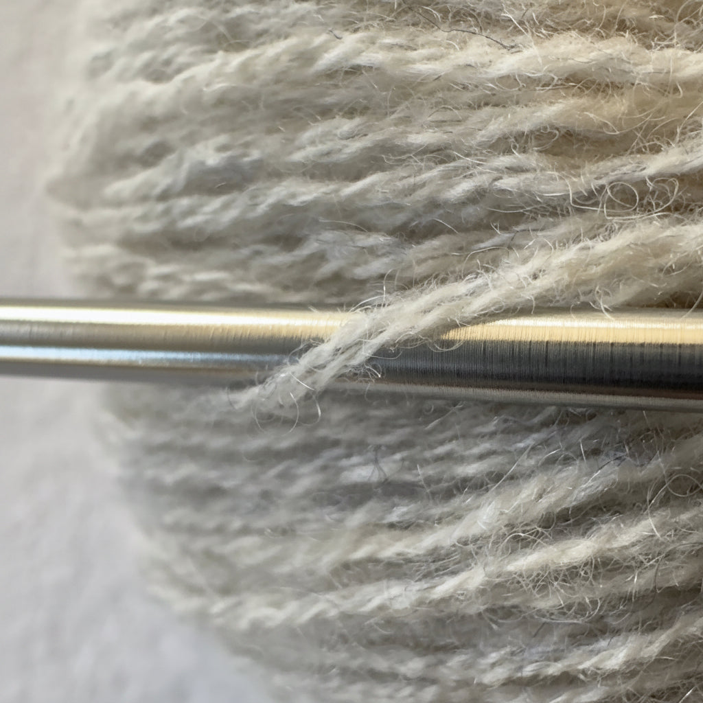 Close-up of fingering weight reclaimed cashmere yarn in Earl Grey, a soft pearl grey tone with fuzzy halo as it wraps around a sleek stainless steel knitting needle.
