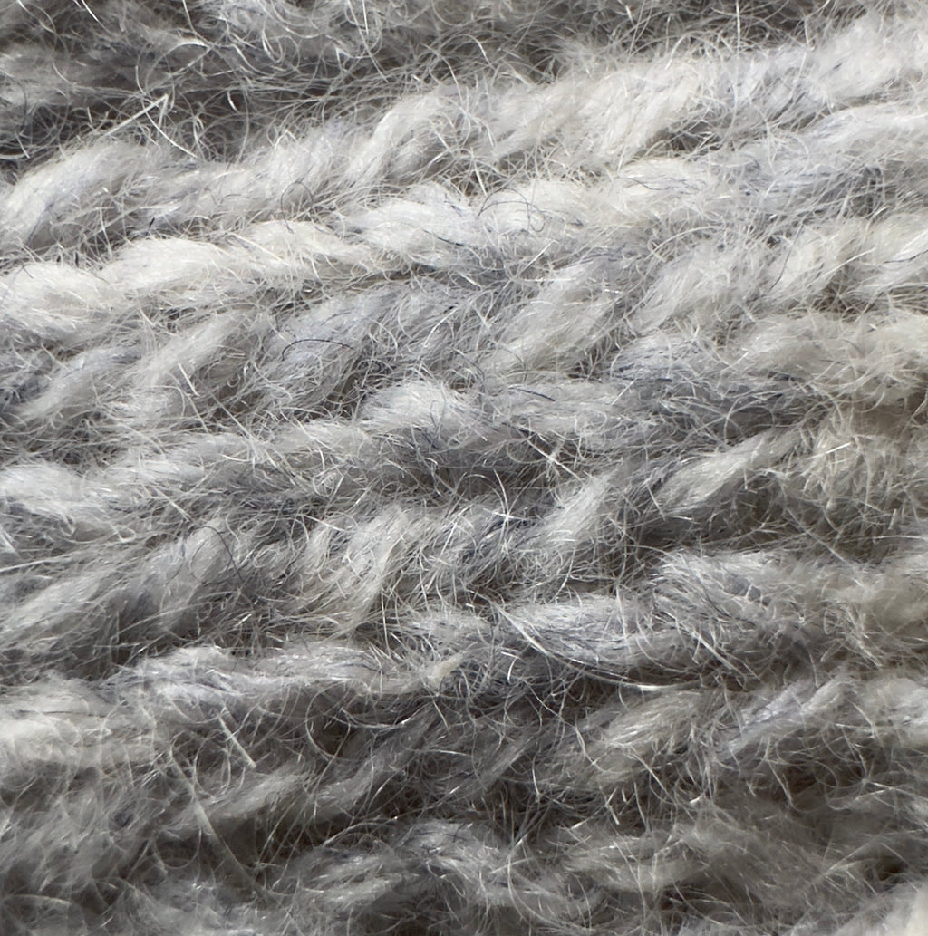 Close-up texture of reclaimed cashmere yarn in a pearl gray color. The soft halo of cashmere fibres is shown in a hand knit stitch pattern.
