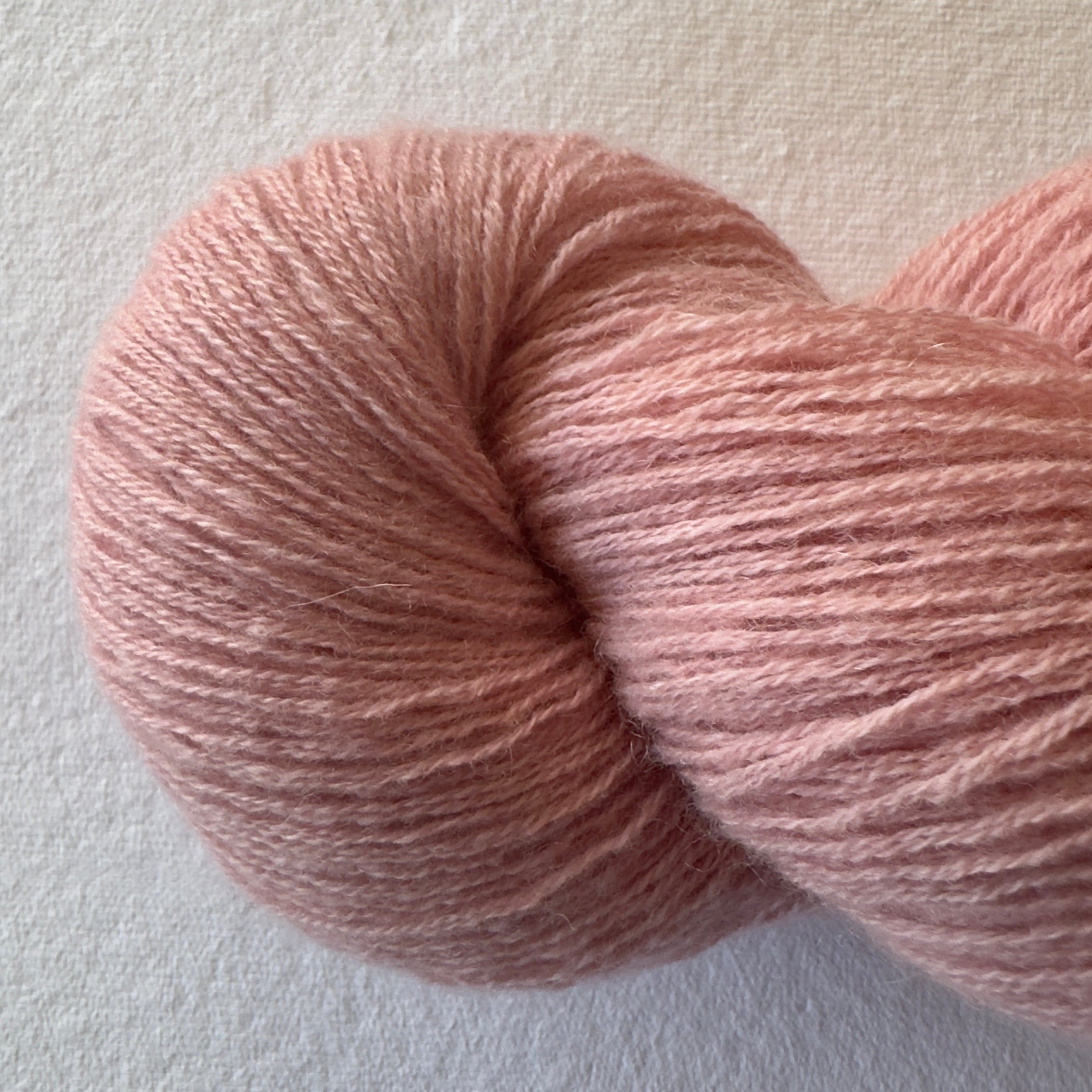 Close-up of bouncy sport weight reclaimed cashmere yarn in Peach Blossom, a vibrant peachy coral tone with plump halo.