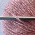 Close-up of bouncy sport weight reclaimed cashmere yarn in Peach Blossom a vibrant coral blush tone with plump halo as it wraps around a sleek stainless steel knitting needle.