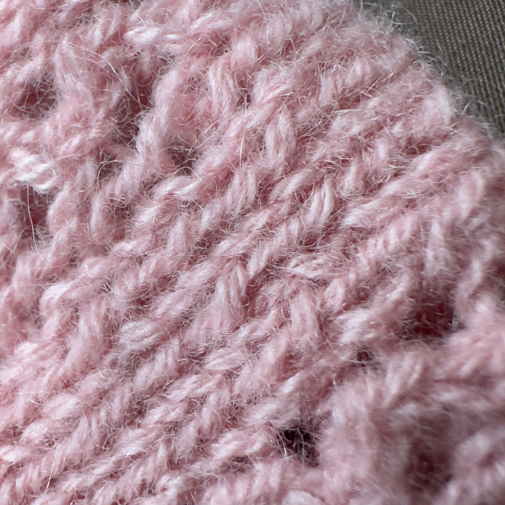 Close-up texture of knitted reclaimed cashmere yarn in a vibrant blush pink color. The soft halo of cashmere fibres in shown against a taupe brown silk background. 
