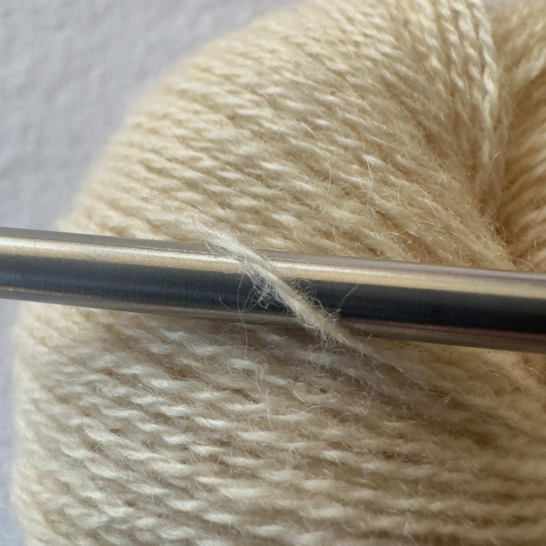 Close-up of lace weight reclaimed cashmere yarn in Raw Honey, a creamy yellow tone with soft halo as it wraps around a sleek stainless steel knitting needle.