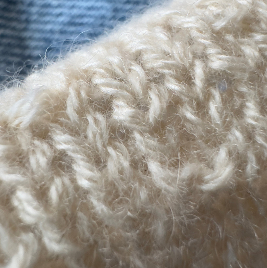 Close-up texture of reclaimed cashmere knit fabric in cream color. The soft halo of cashmere fibres is shown against a light blue denim background. 