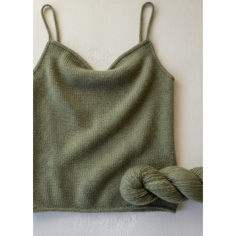 Close-up of a hand knit cashmere camisole alongside a twisted skein of reclaimed cashmere yarn in a matching earthy, muted sage green color. The texture of the yarn looks soft and luxurious against a cream cotton background.