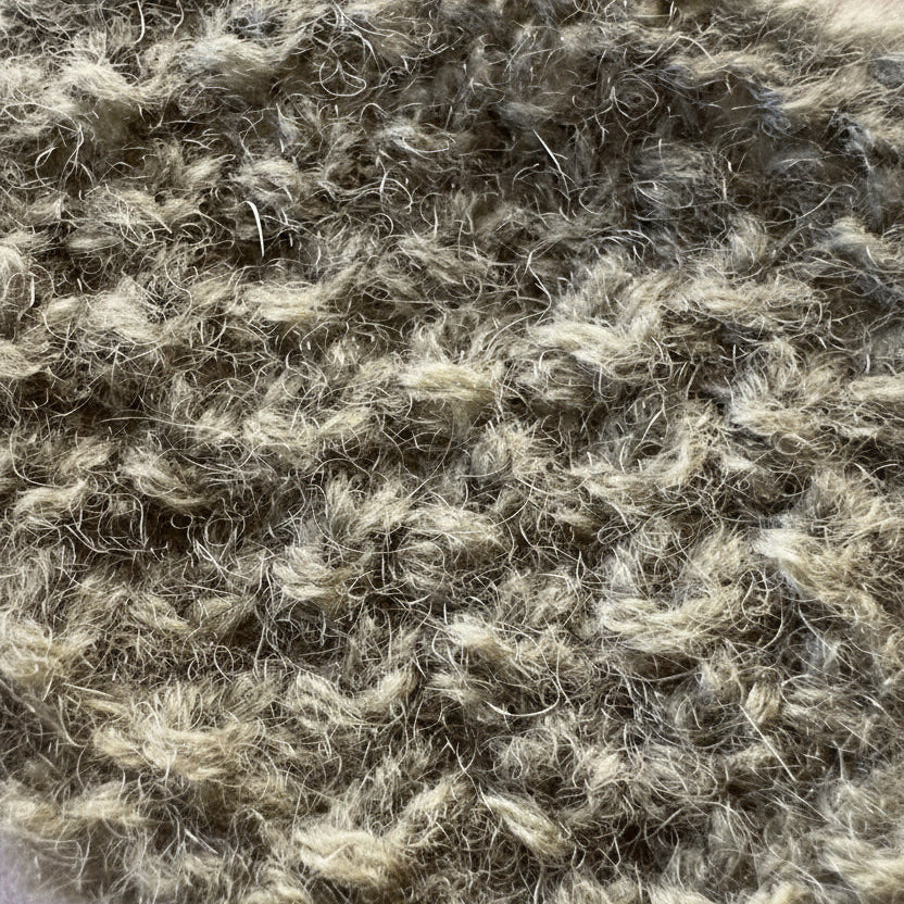 Close-up texture of knitted reclaimed cashmere yarn in a muted earthly sage green color. The soft halo of cashmere fibres is shown against a cream linen background.